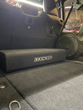Close side view of the Down-Firing CompRT Kicker subwoofer enclosure installed in the trunk of a Jeep, showcasing its compact, thin-profile design and durable build