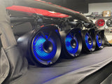 Four black JBL MT8HLB 8-inch marine tower speakers installed on a boat, illuminated with blue RGB LED lights, showcasing their powerful audio and sleek design