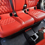 View of the BRP JT Gladiator underseat subwoofer enclosure, partially covered by red seats, with only a small portion of the enclosure visible after installation